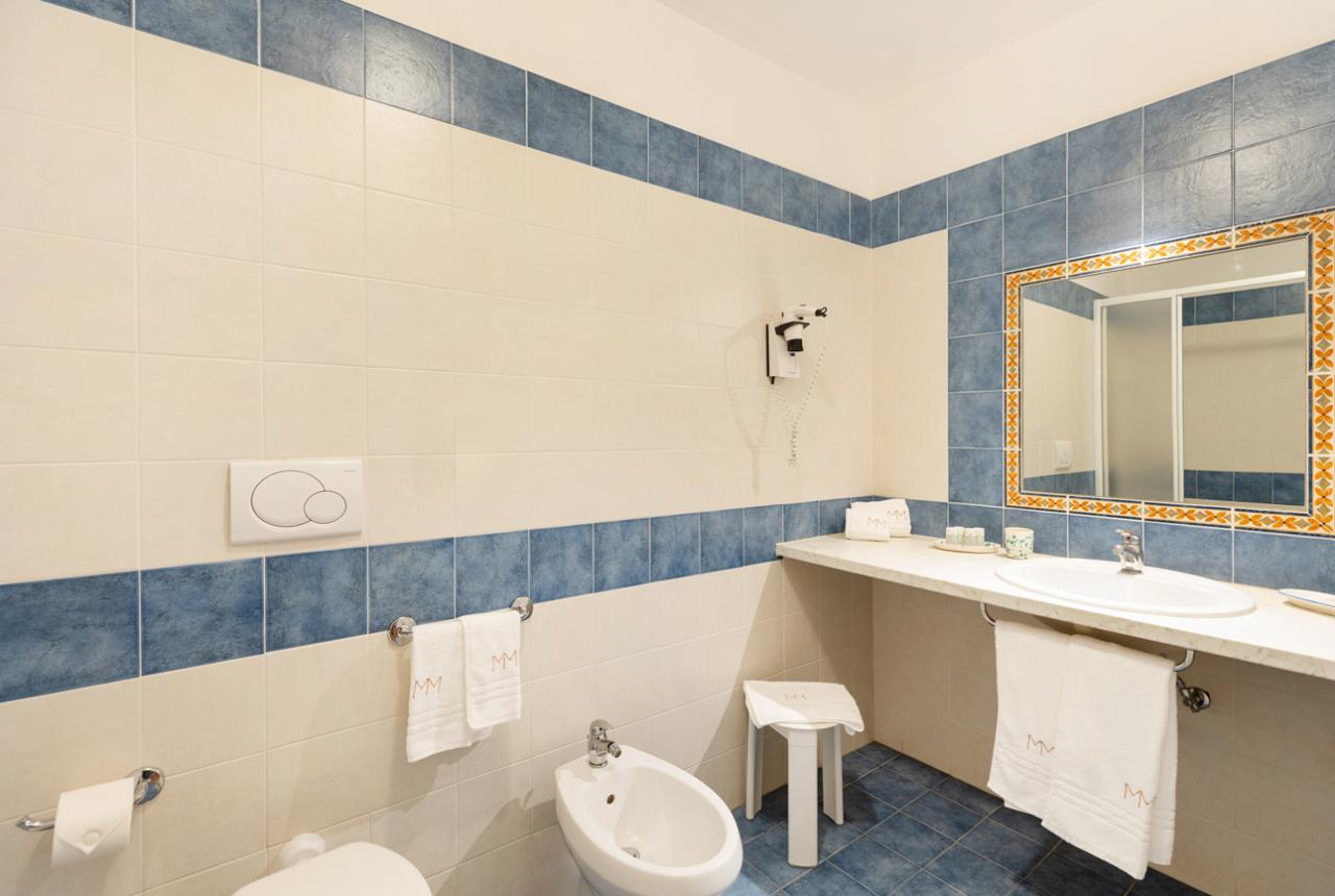 Bagno elegante con piastrelle blu e bianche, specchio decorato e asciugamani bianchi.