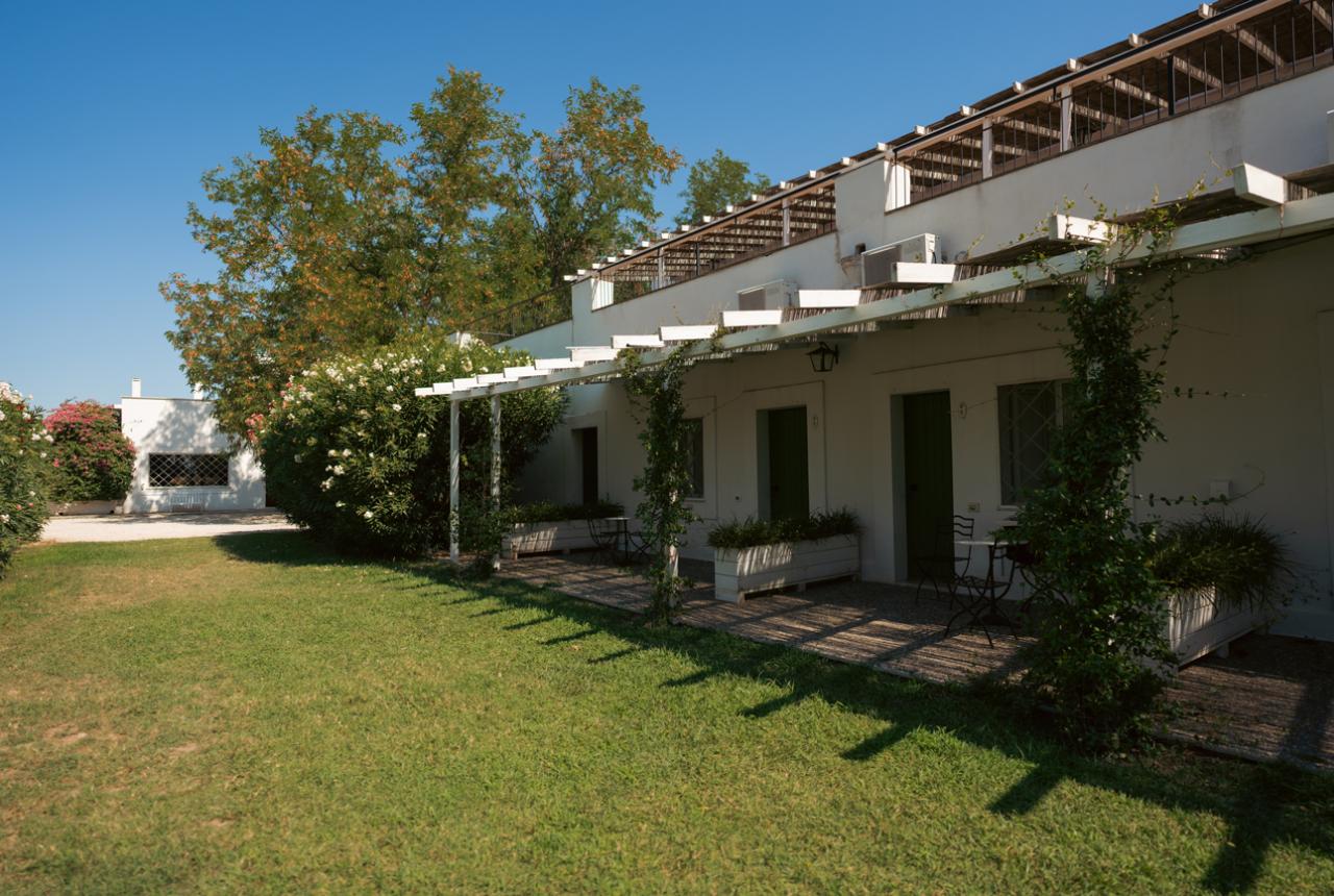 Casa bianca con pergolato e giardino verde sotto un cielo azzurro.