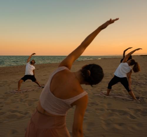 Gruppo di persone fa yoga sulla spiaggia al tramonto.