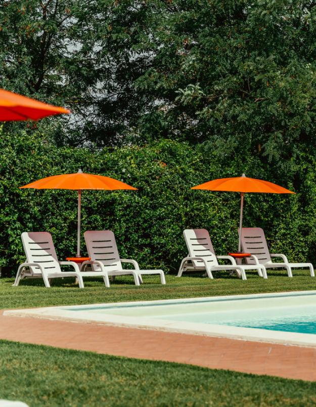 Piscina all'aperto con lettini e ombrelloni arancioni su prato verde.
