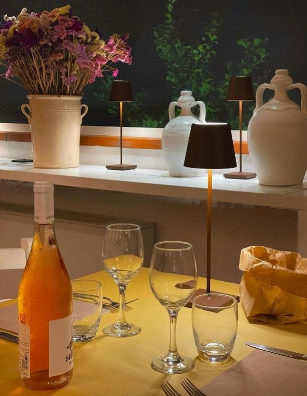 Tavola apparecchiata con bottiglia di vino, bicchieri e decorazioni floreali.