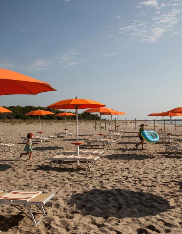 Spiaggia con ombrelloni arancioni, lettini e alcune persone sullo sfondo.
