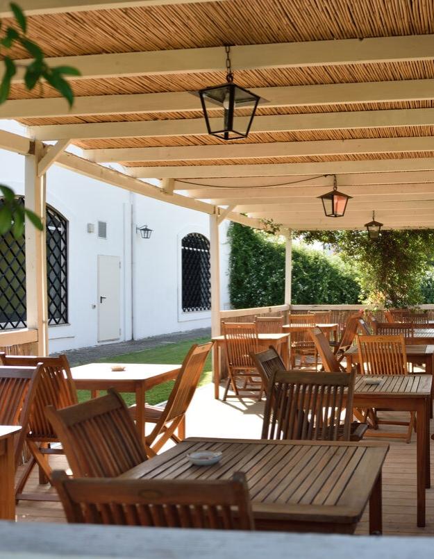 Terrazza all'aperto con tavoli e sedie in legno, coperta da pergolato.