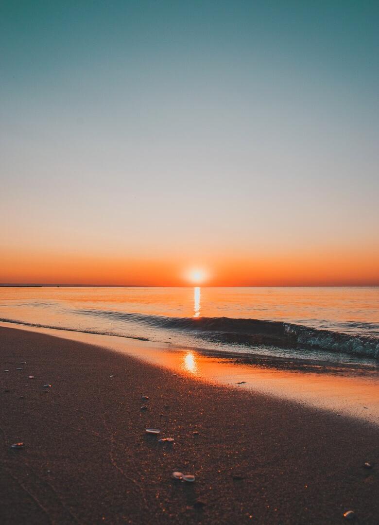Tramonto sereno sul mare con riflessi arancioni sulla spiaggia.